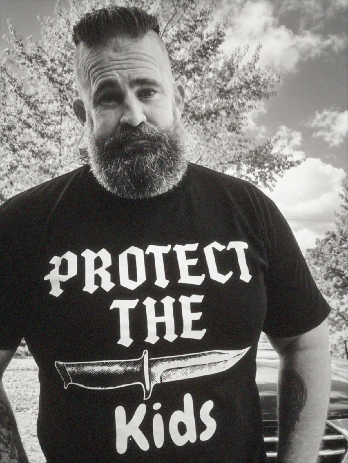 Community member wearing a Protect the Kids shirt in a grainy black and white outdoor photo